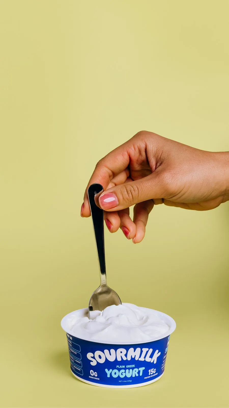A hand dipping a spoon into a cup of Sourmilk
